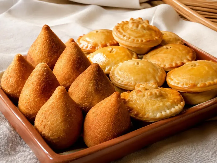 Coxinhas e empadas douradas em uma travessa de cerâmica